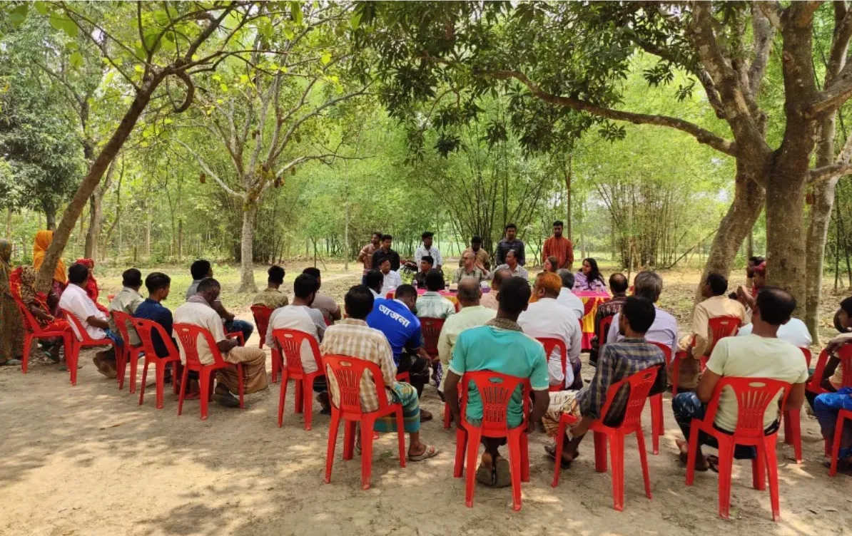 Group of cotton farmers seated with CottonConnect staff at an engagement session in Chuadanga, reviewing printed bulletin material together.