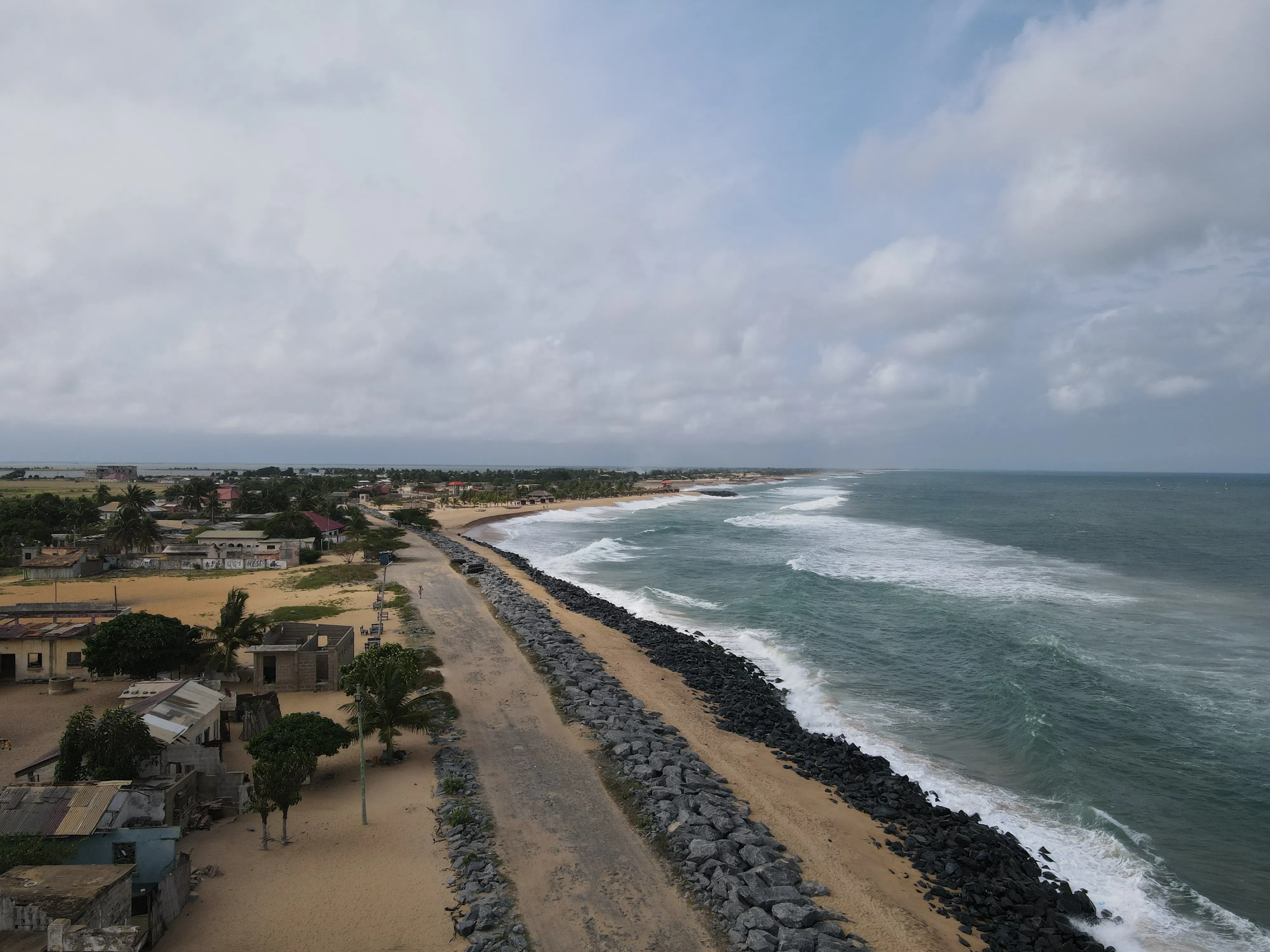 Rock revetment and sea defence structures running along the shoreline at Keta, with waves breaking against them.